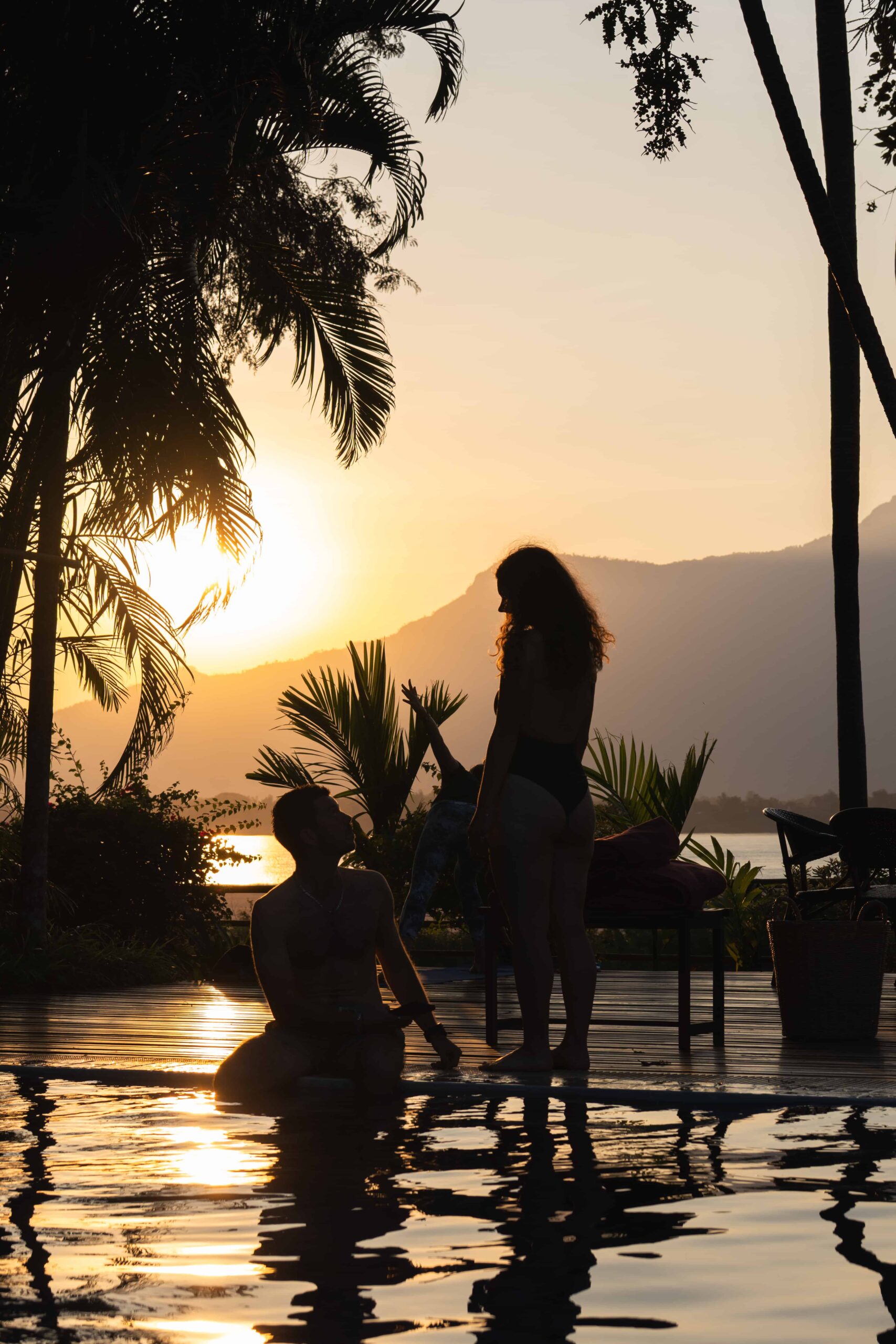 Two guests in the pool at sunset with the Mekong and mountains beyond