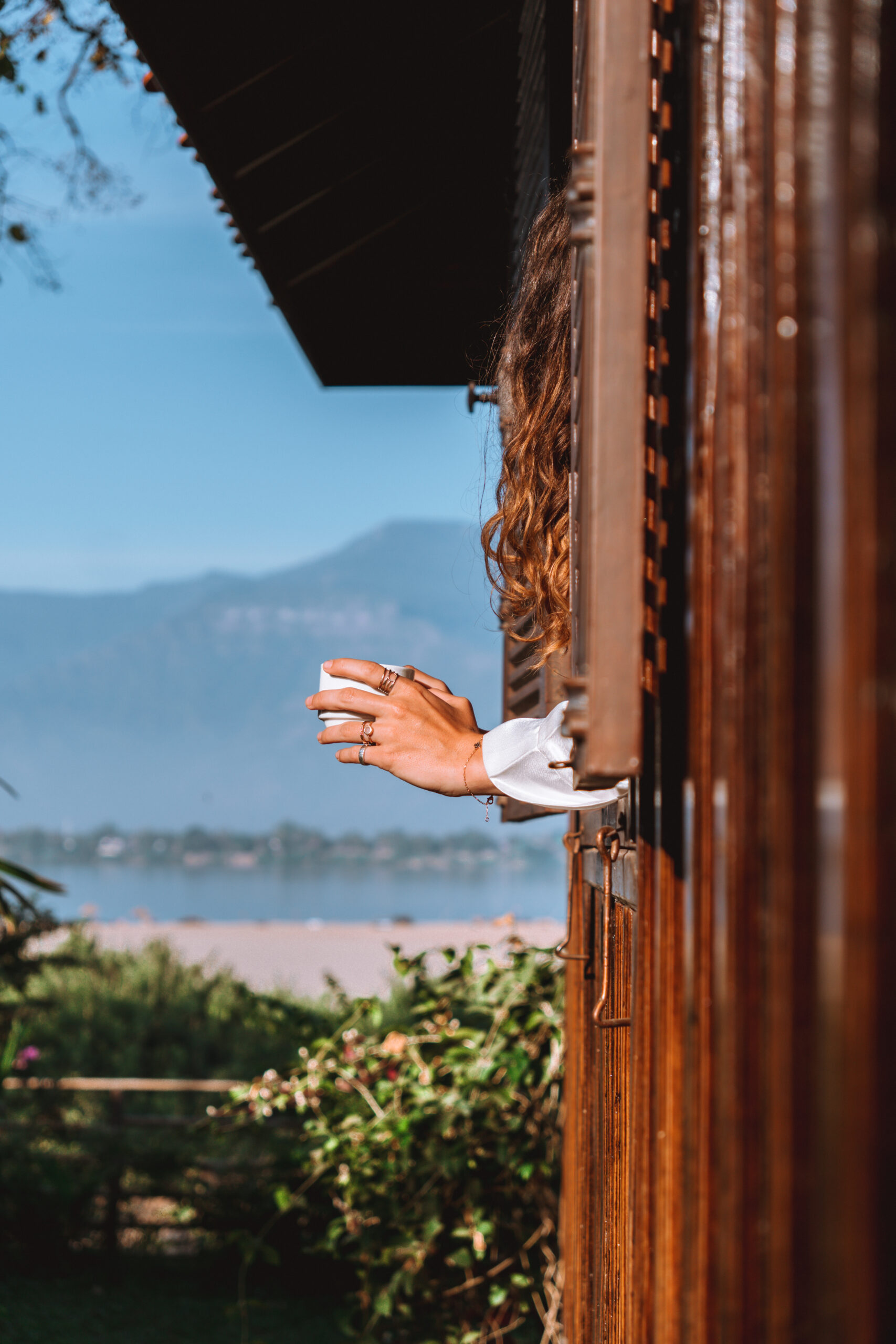 A guest reaching from a timber doorway towards the river and distant mountains