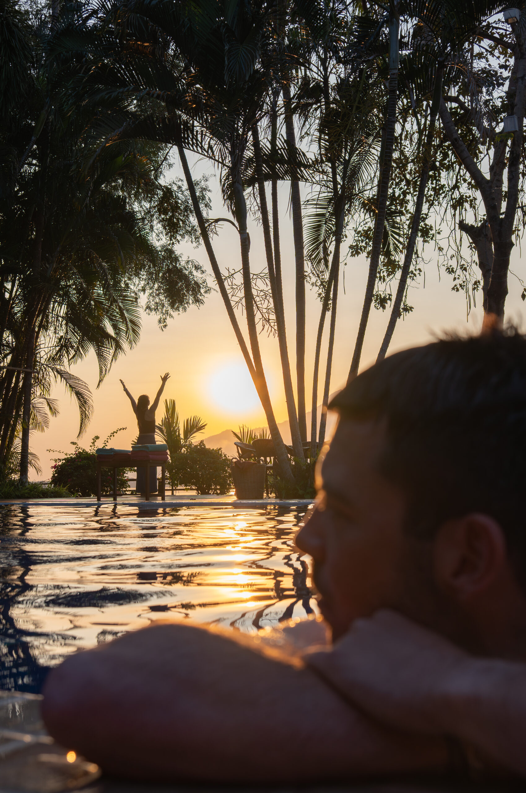 A guest resting at the edge of the pool as the sun sets behind the trees