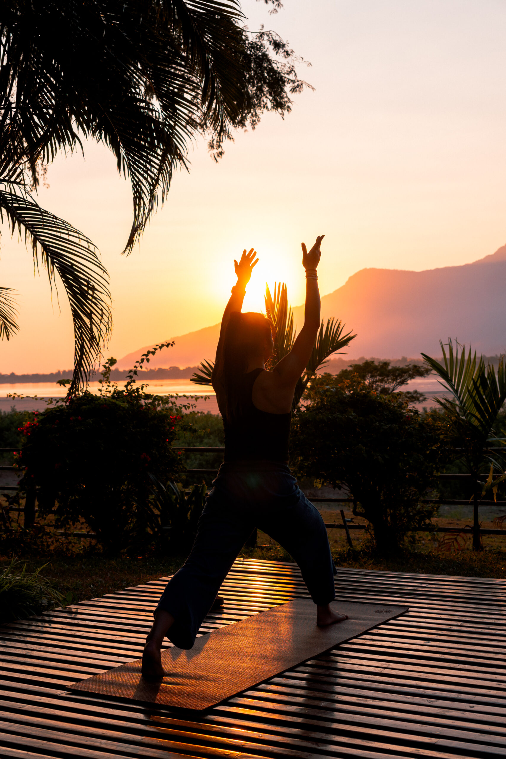 A person holding a yoga pose on a wooden deck at sunset